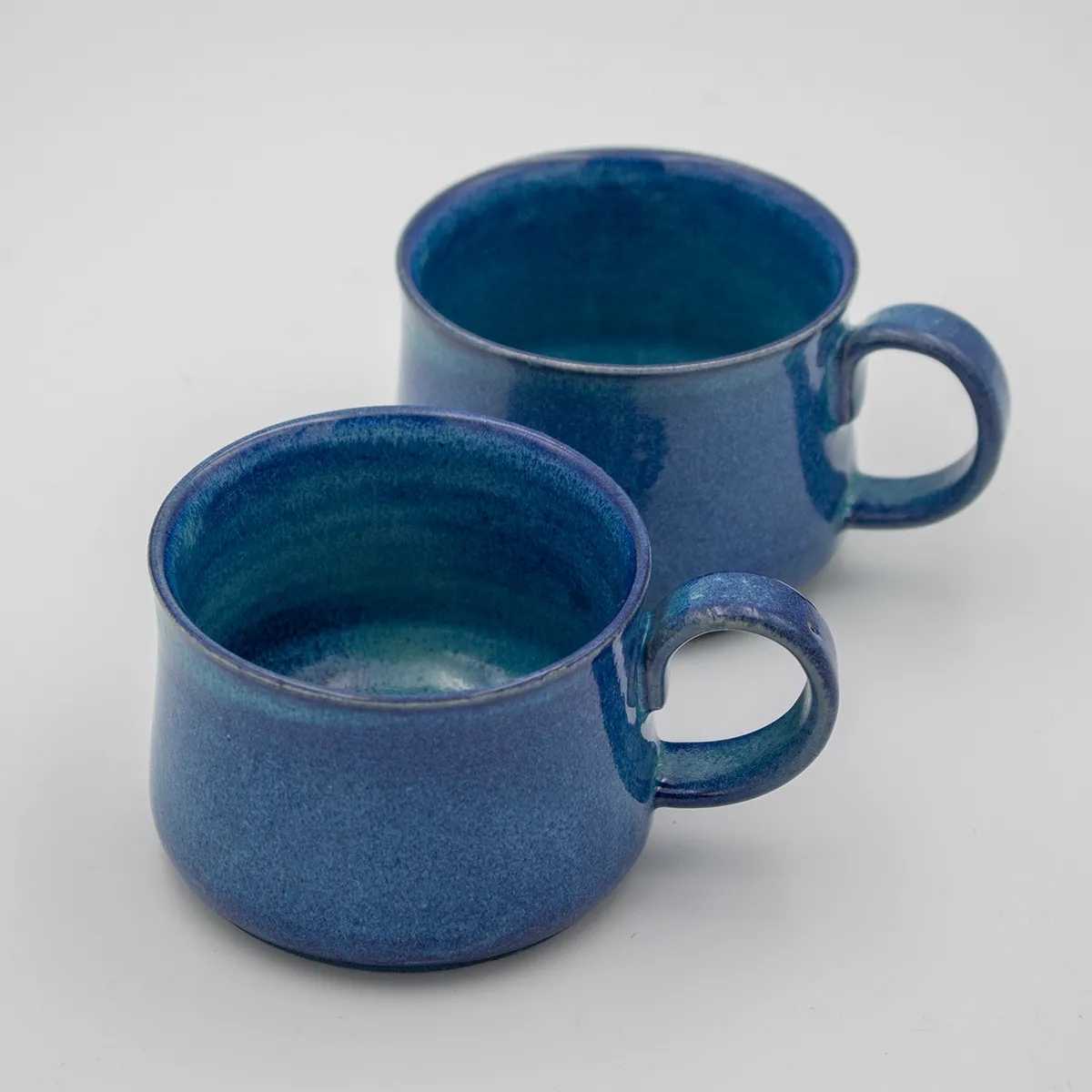 Two hand-thrown mugs in a mottled blue glaze, low and wide with round pulled handles